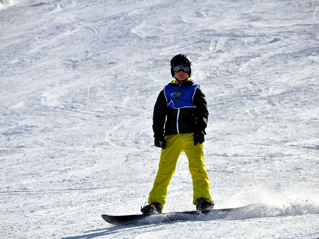 Snowboarder in gelber Hose steht am Hang.
